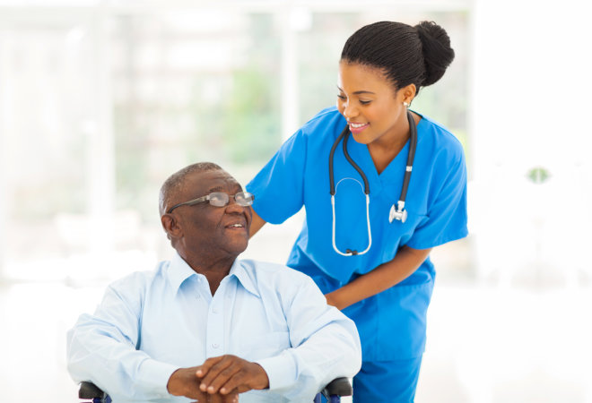 Elderly man in a wheelchair and female nurse assisting