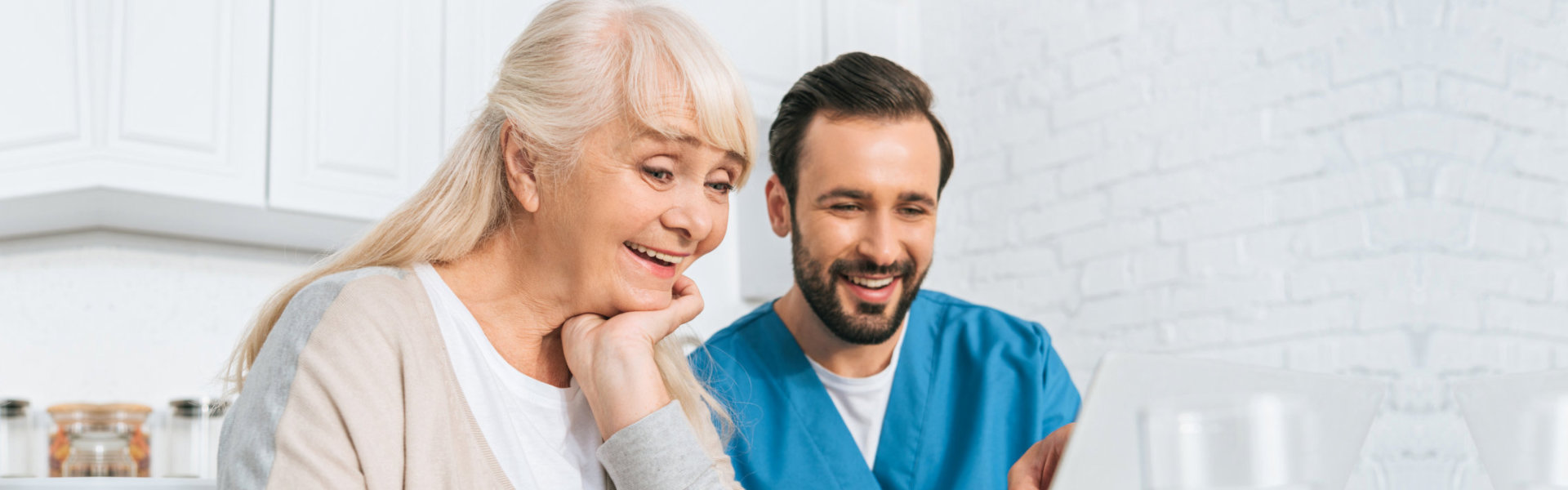 Elderly and nurse smiling while looking at the laptop